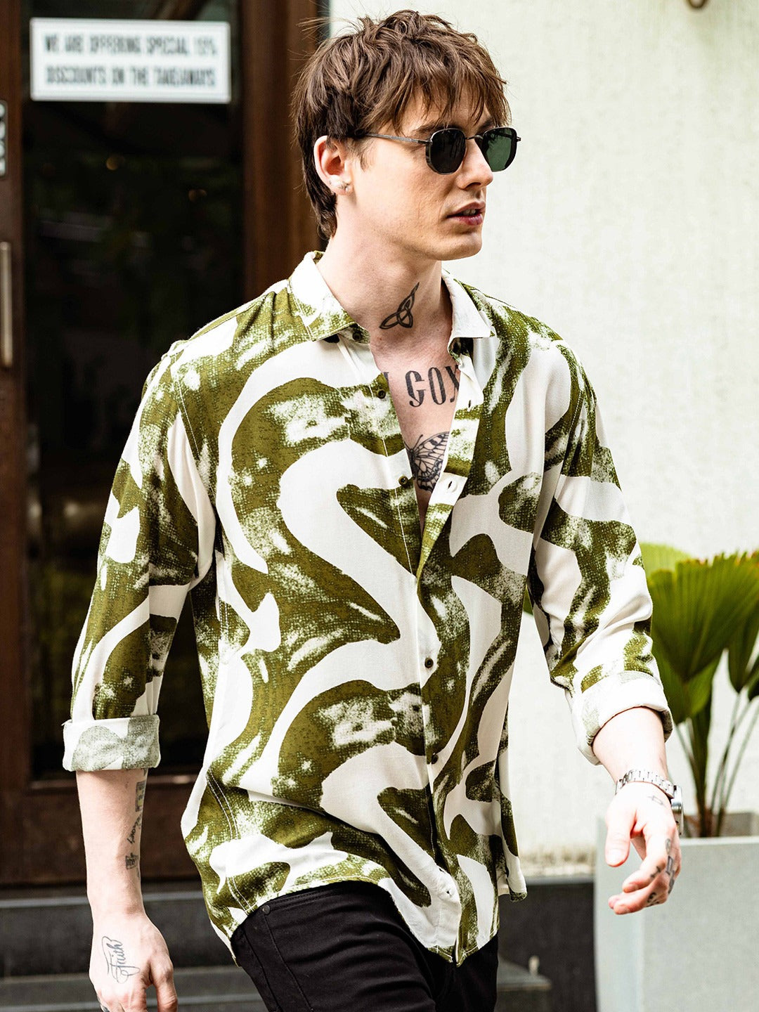 Person wearing a green and white patterned shirt with tattoos visible on arms and neck.