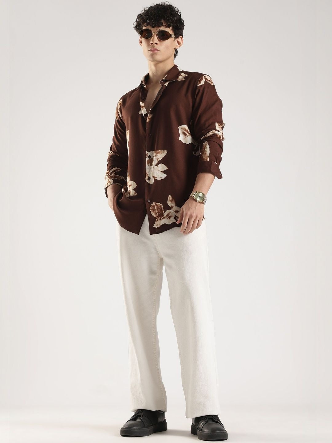 Man wearing a brown floral shirt and white pants on a white background