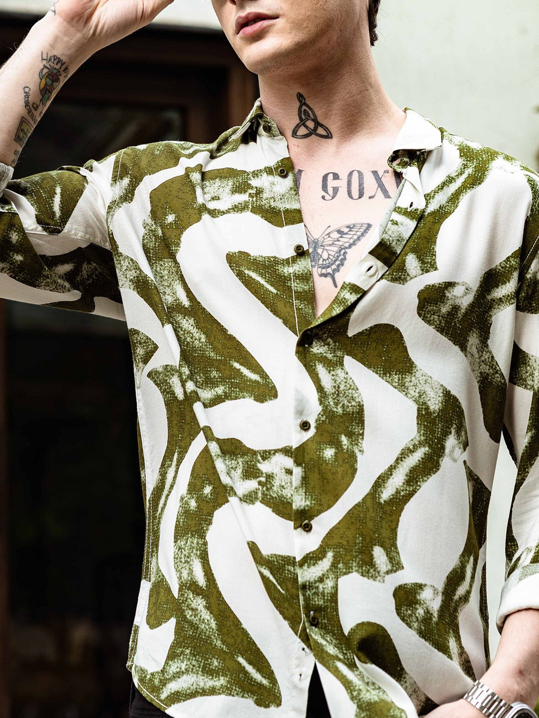 Person wearing a patterned shirt with visible tattoos and jewelry.