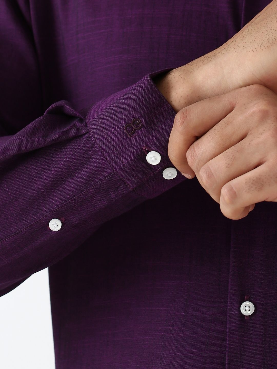 Close-up of a person adjusting the cuff of a purple shirt with white buttons.