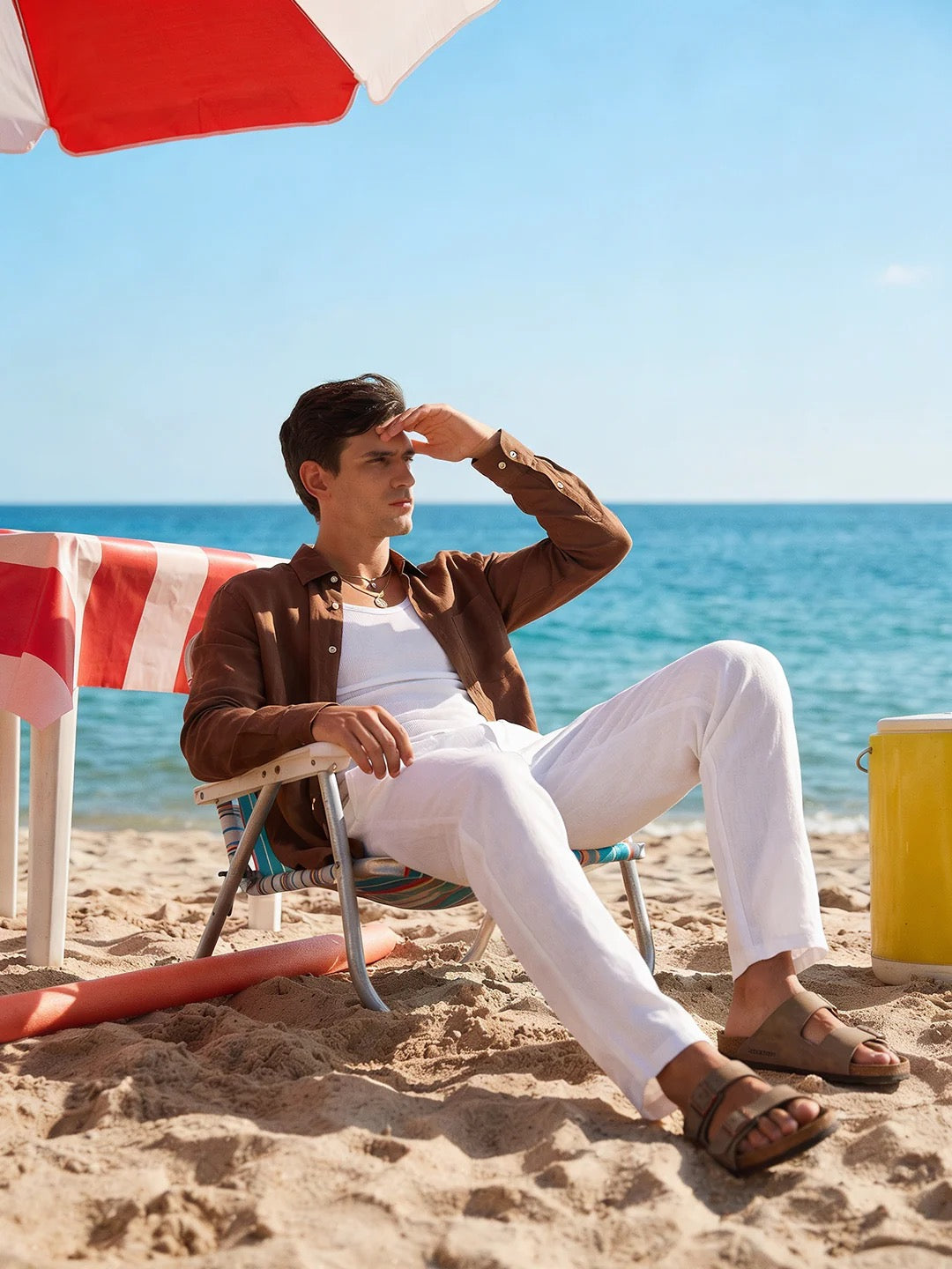 Man sitting on a beach chair under an umbrella with ocean in the background