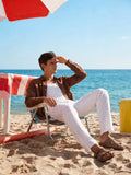 Man sitting on a beach chair under an umbrella with ocean in the background