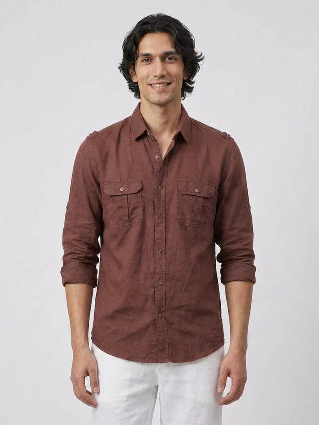 Man wearing a brown button-up shirt and white pants on a plain background