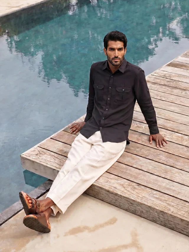 Man sitting by a pool wearing a black shirt and white pants.