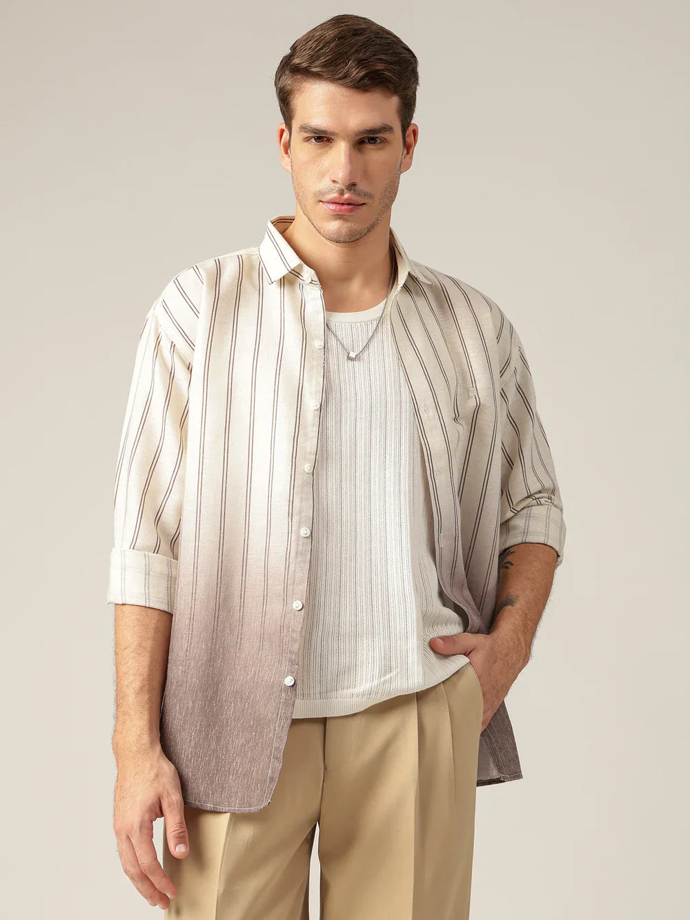 Man wearing a striped shirt over a white undershirt with beige pants on a plain background