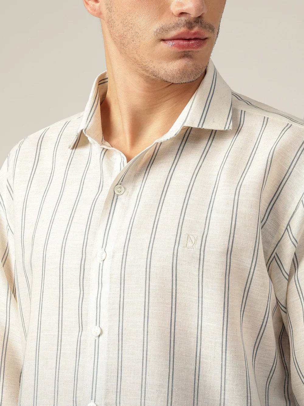 Man wearing a beige and gray striped shirt with a brand logo on a neutral background