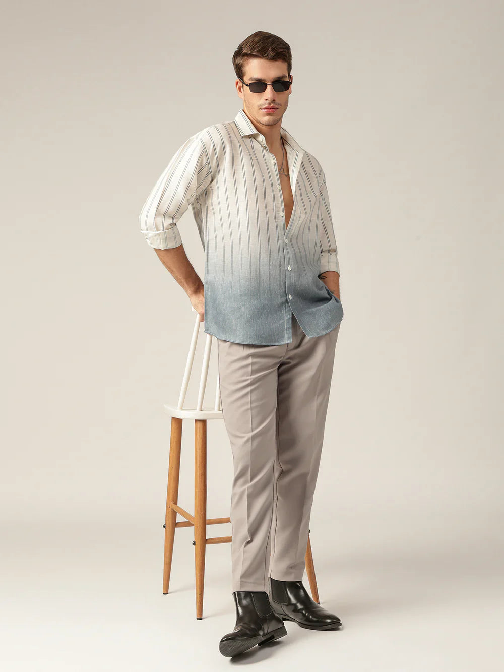 Man wearing a striped shirt with a gradient effect and beige pants, standing against a plain background.
