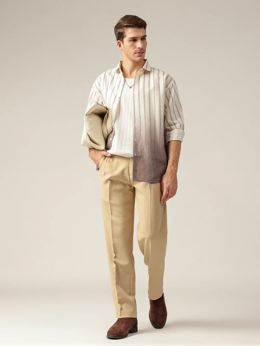 Man wearing a striped shirt with a beige jacket and pants on a plain background