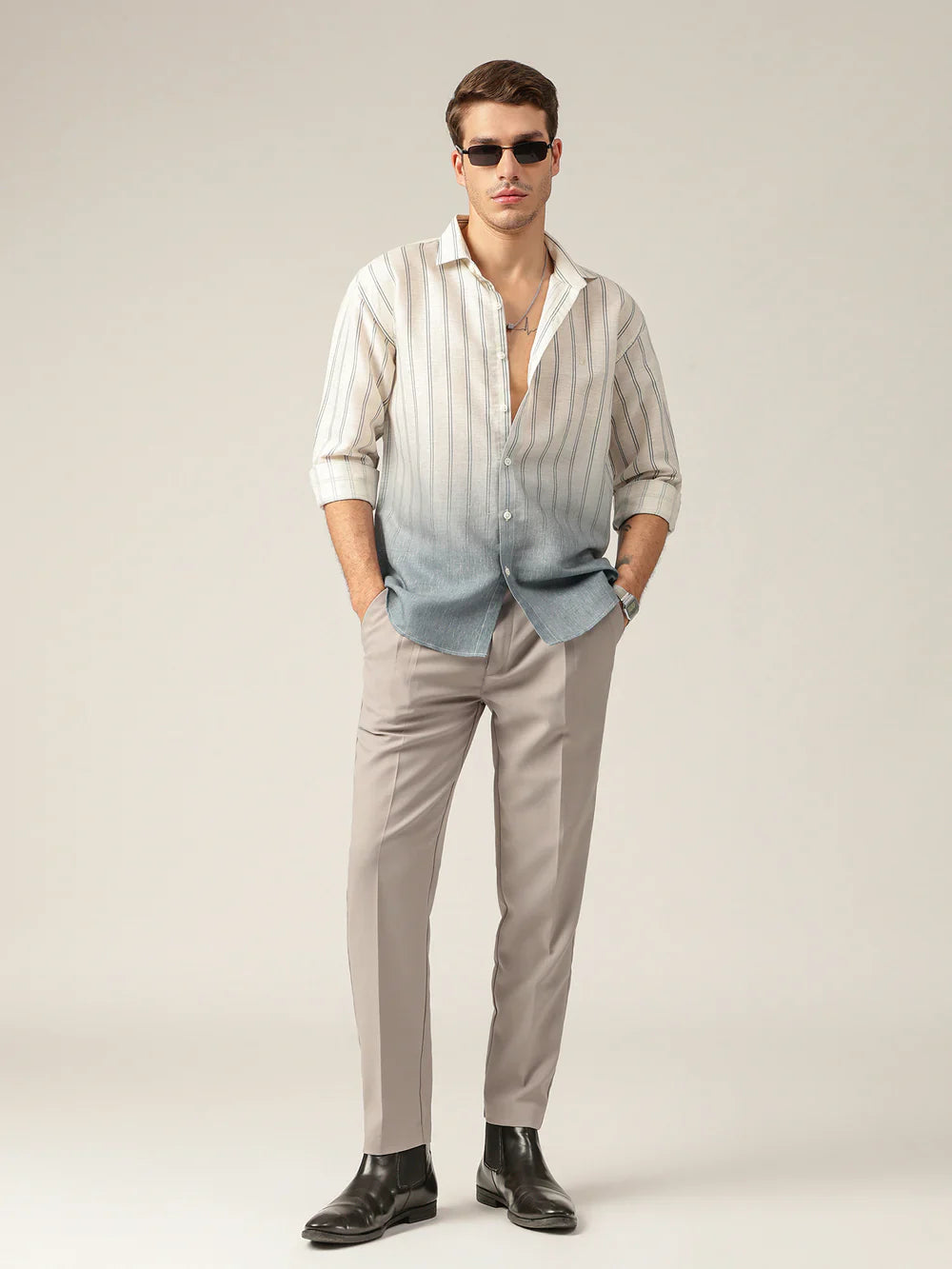 Man wearing a striped shirt, light gray pants, and dark shoes on a plain background