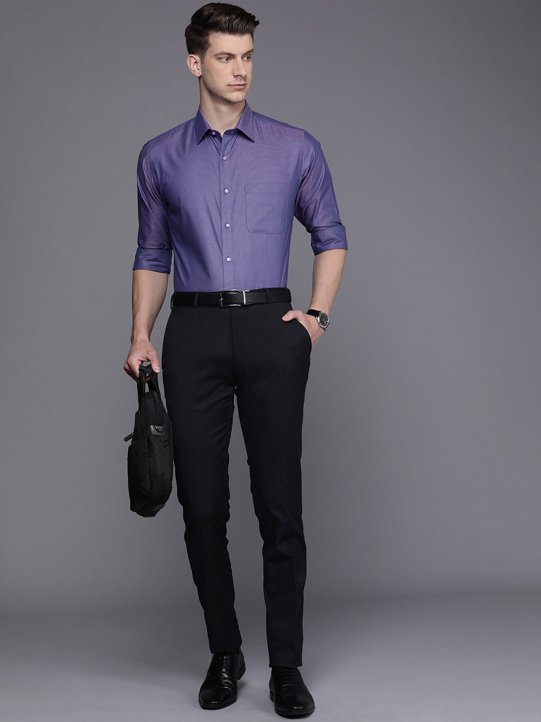 Man wearing a purple dress shirt and black pants against a gray background