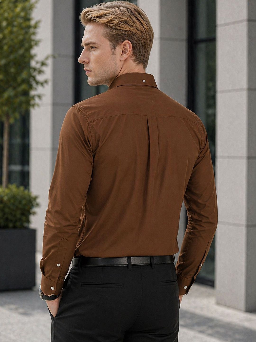 Man wearing a brown shirt and black pants standing outdoors.
