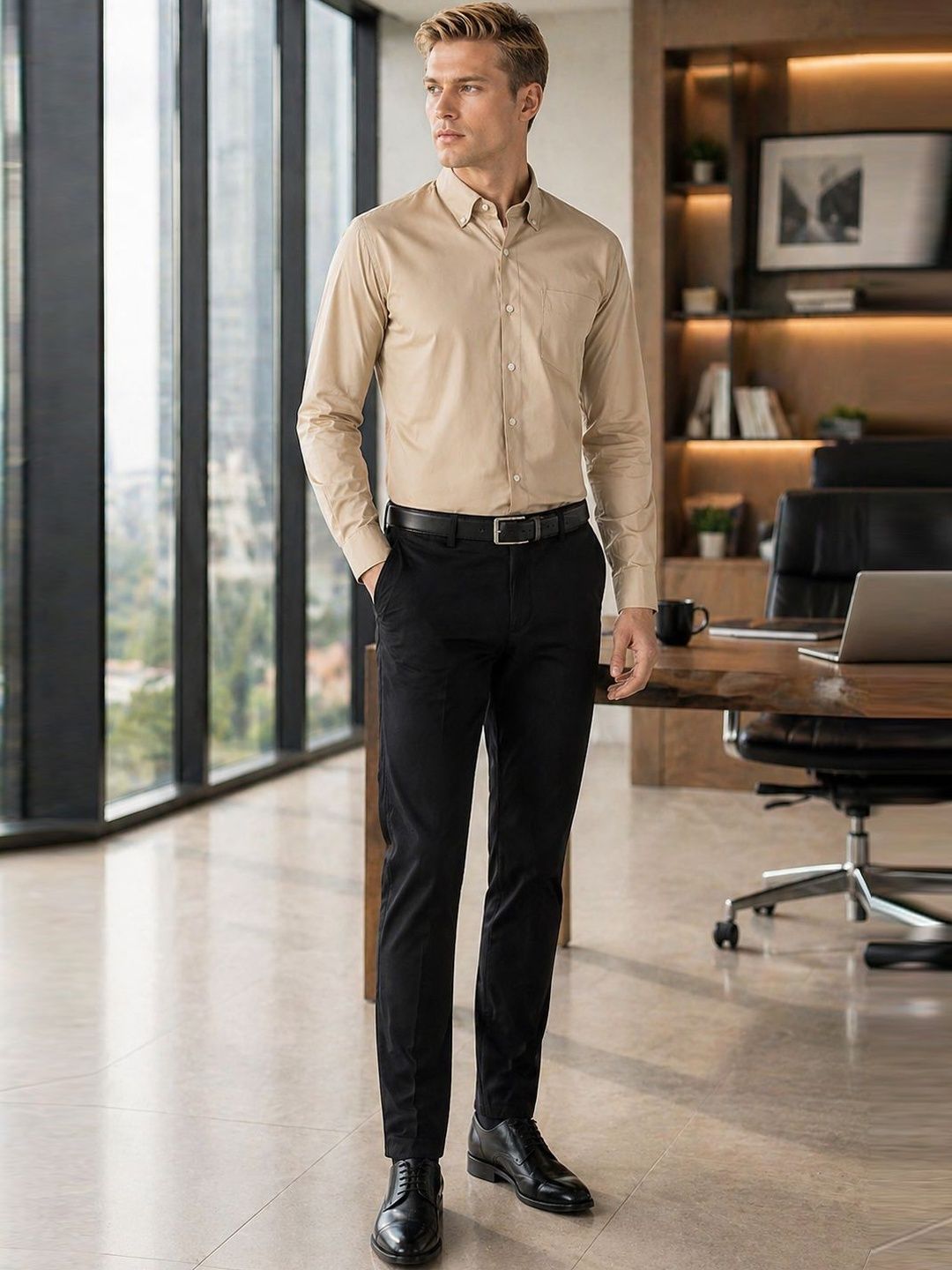 Man in a beige shirt and black pants standing in an office setting.