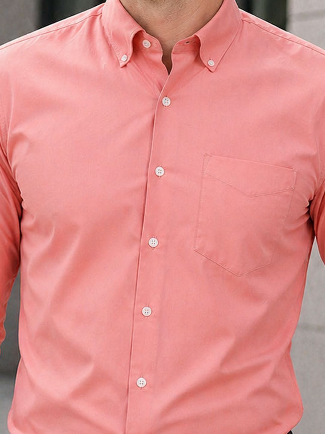 Close-up of a person wearing a pink button-up shirt with a neutral background