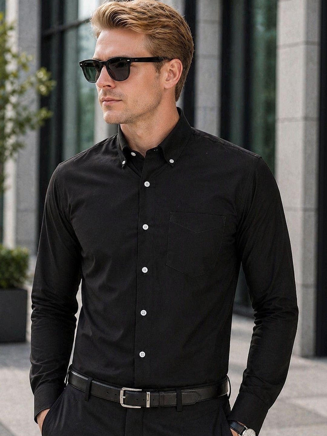 Man wearing a black dress shirt and sunglasses outdoors.