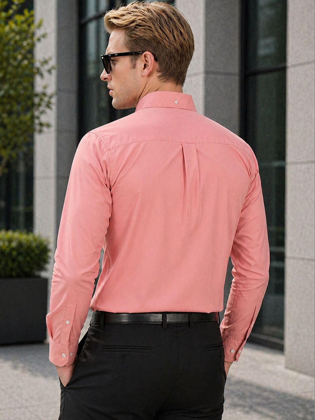 Man wearing a pink shirt and black pants standing outdoors near a building.