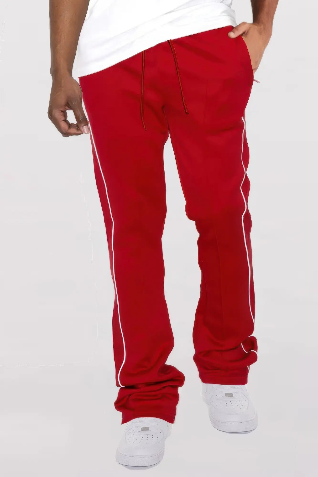 Red track pants with white stripes worn by a person on a light gray background