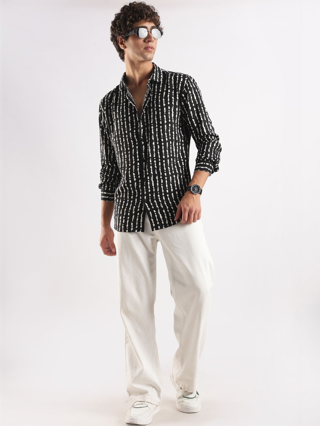 Man wearing a black and white patterned shirt with white pants on a white background