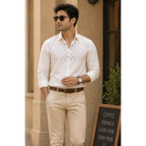 Man wearing a white patterned shirt and beige pants standing outdoors.