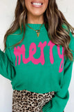 A woman wearing a bright green knit sweater with the word 'merry' in large hot pink letters across the chest, paired with a leopard-print skirt and gold necklaces.