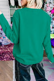 A woman wearing a vibrant green knit sweater and dark jeans, shown from behind in a decorated indoor setting with a Christmas tree in the background.