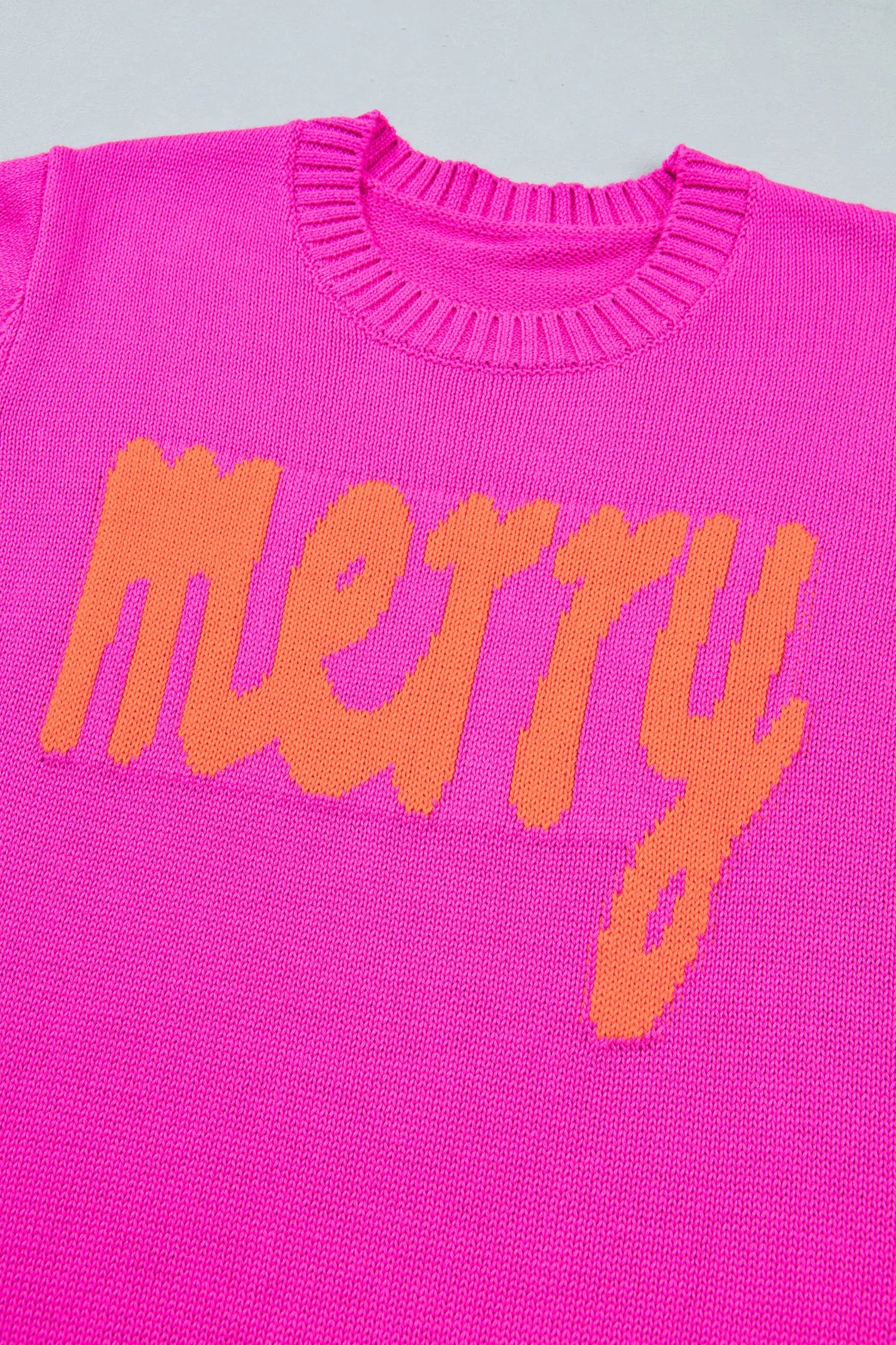 Bright pink knit sweater with “Merry” knitted in orange across chest.