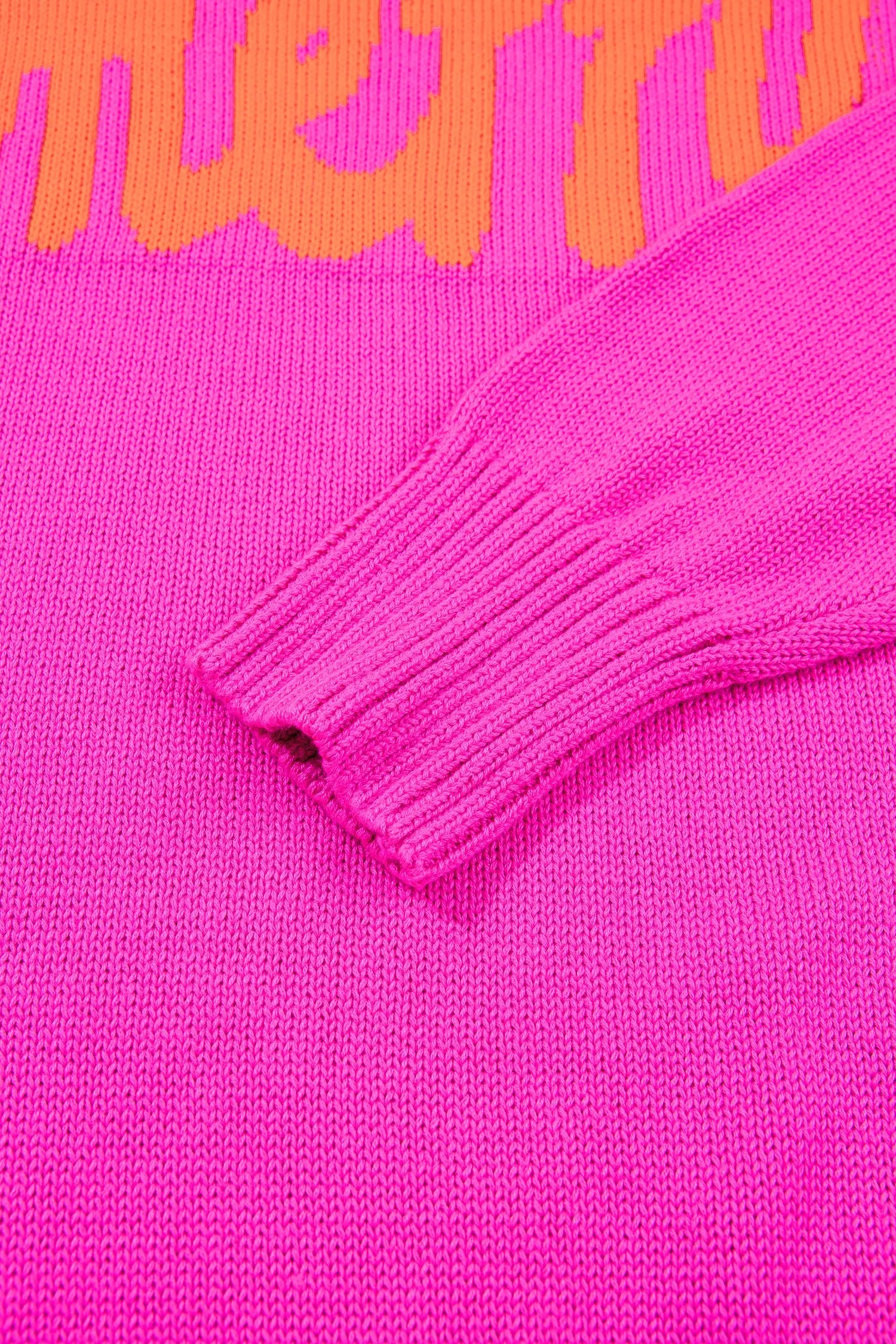 Close-up of a bright pink knit sweater with an orange graphic text detail at the top and a ribbed cuff.