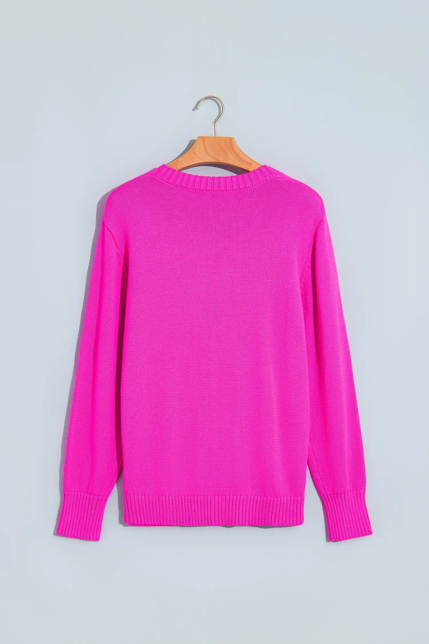 A bright pink long-sleeve knit sweater hanging on a wooden hanger against a light gray background.