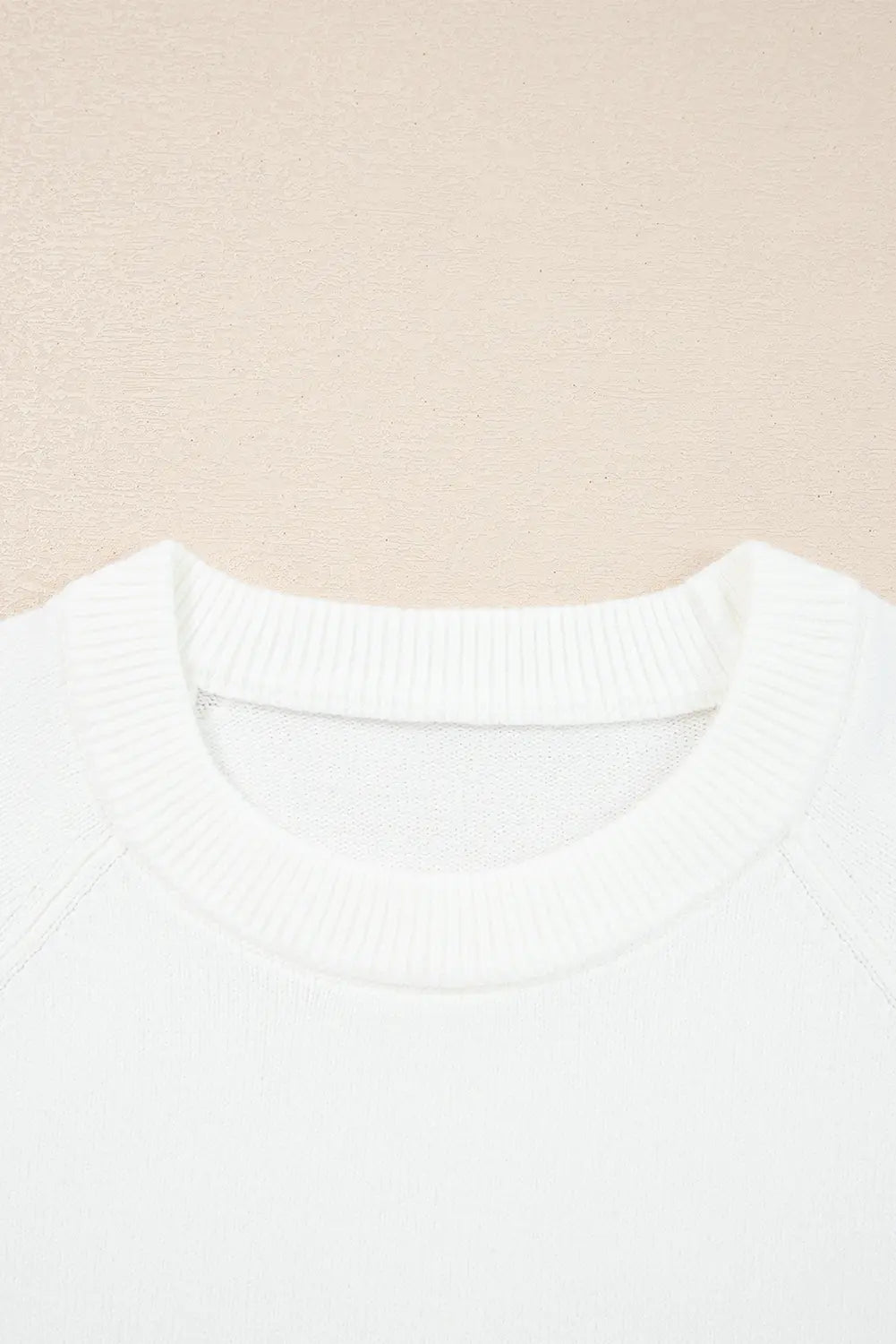 Close-up of a white ribbed crewneck sweater against a light beige textured background.