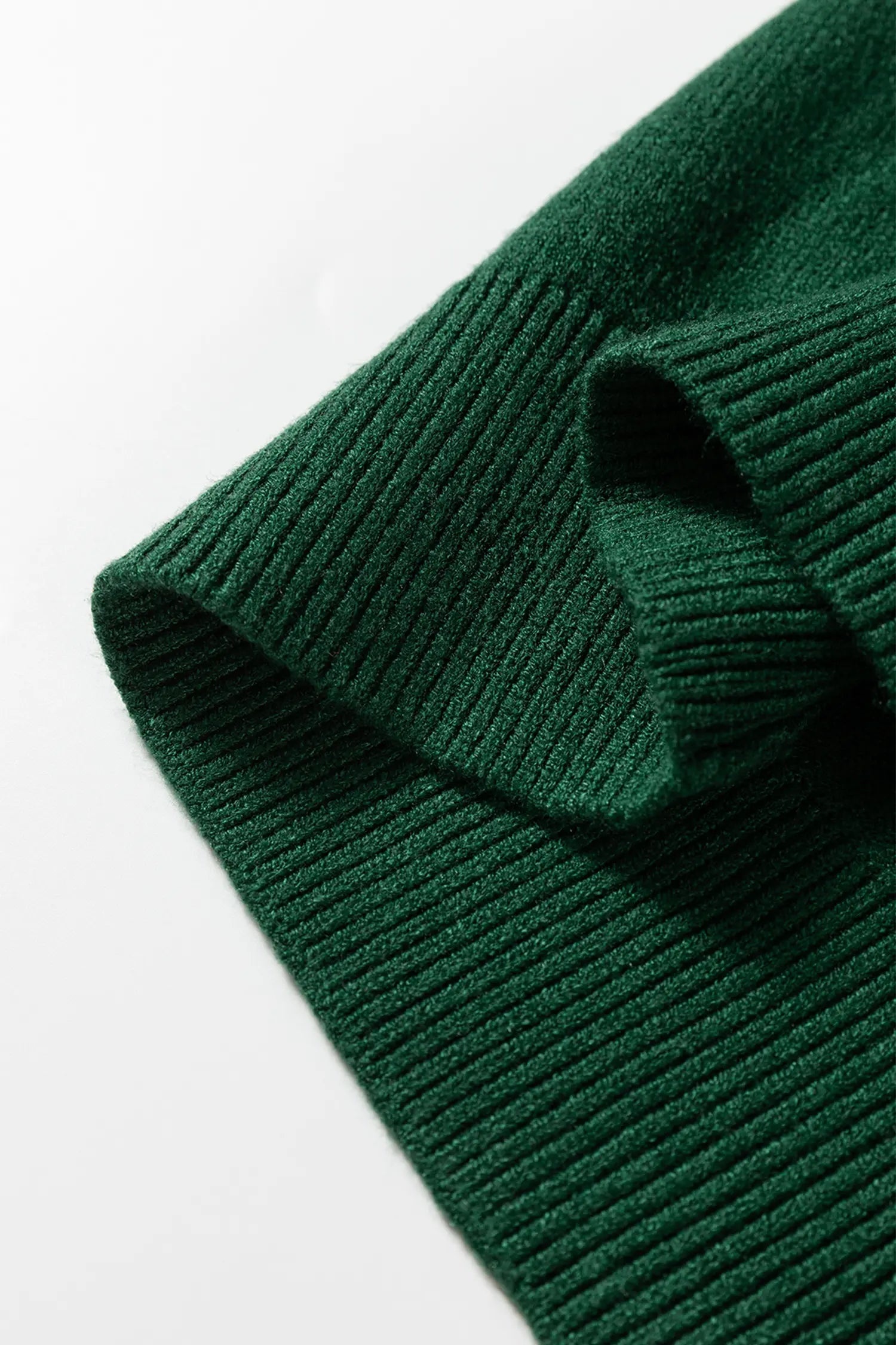 A close-up of a dark forest green ribbed knit fabric, showing the texture and folded edges against a plain white background.