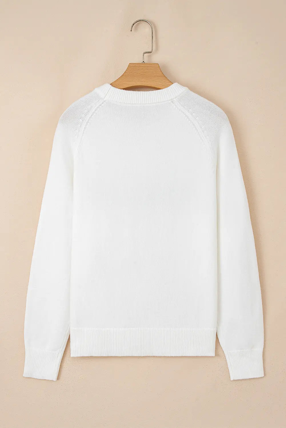 A white long-sleeve knit sweater hanging on a wooden hanger against a solid beige background.