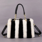 Black and white striped handbag with fur trim on a gray background