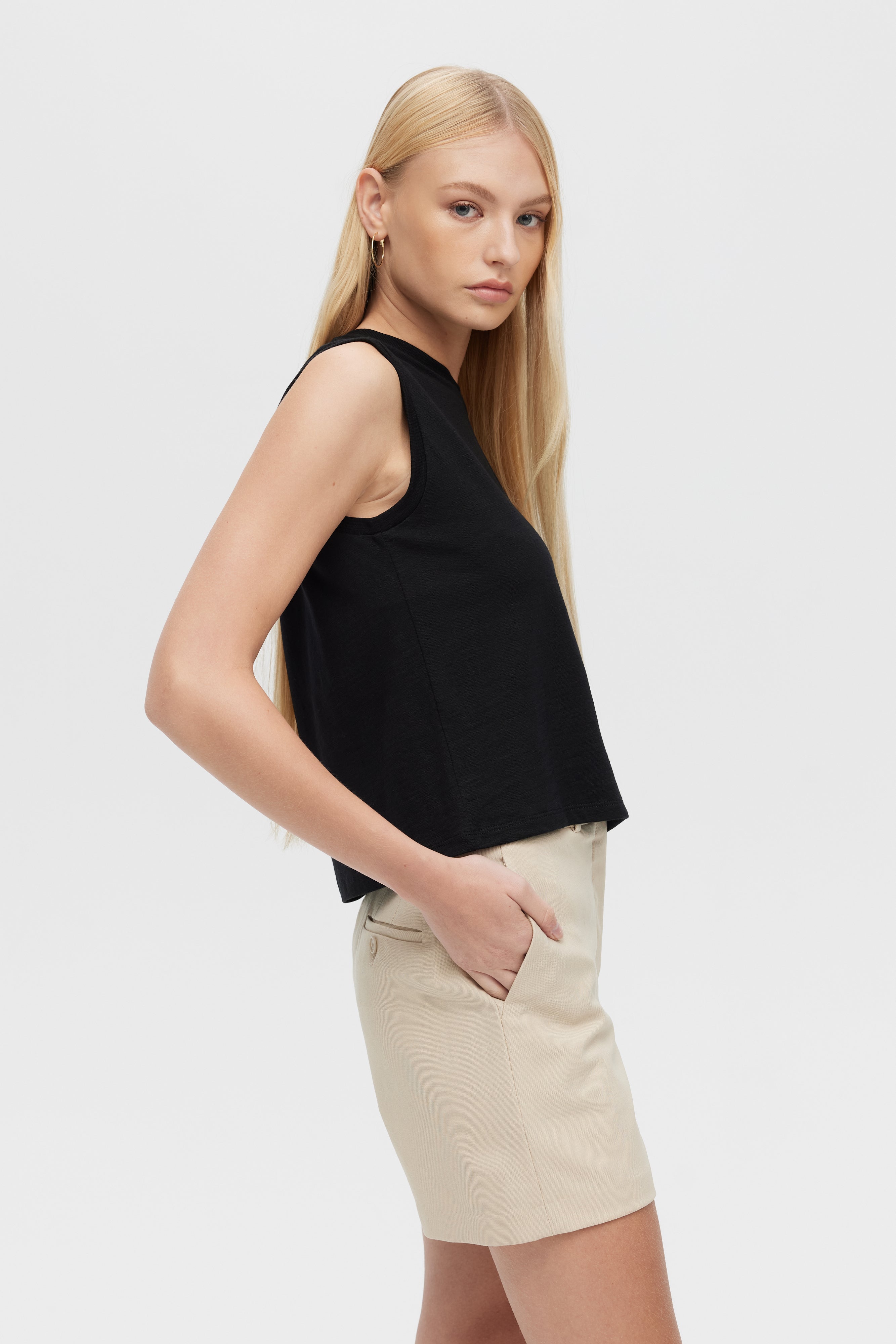 Woman wearing a black sleeveless top and beige shorts on a white background