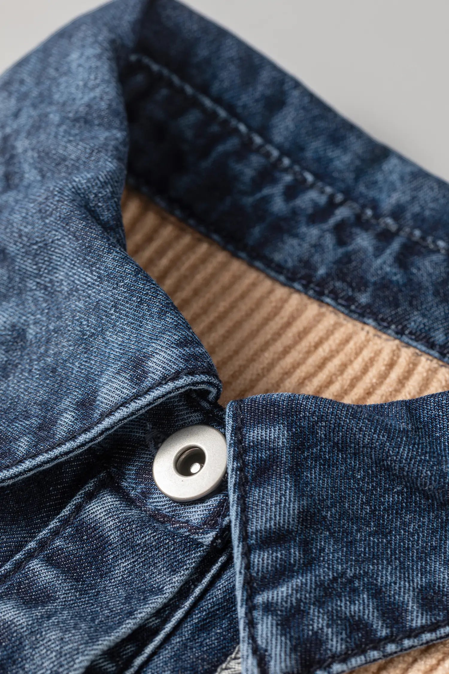 Close-up detail of a dark blue denim jacket showing the collar, button, and a tan ribbed lining.