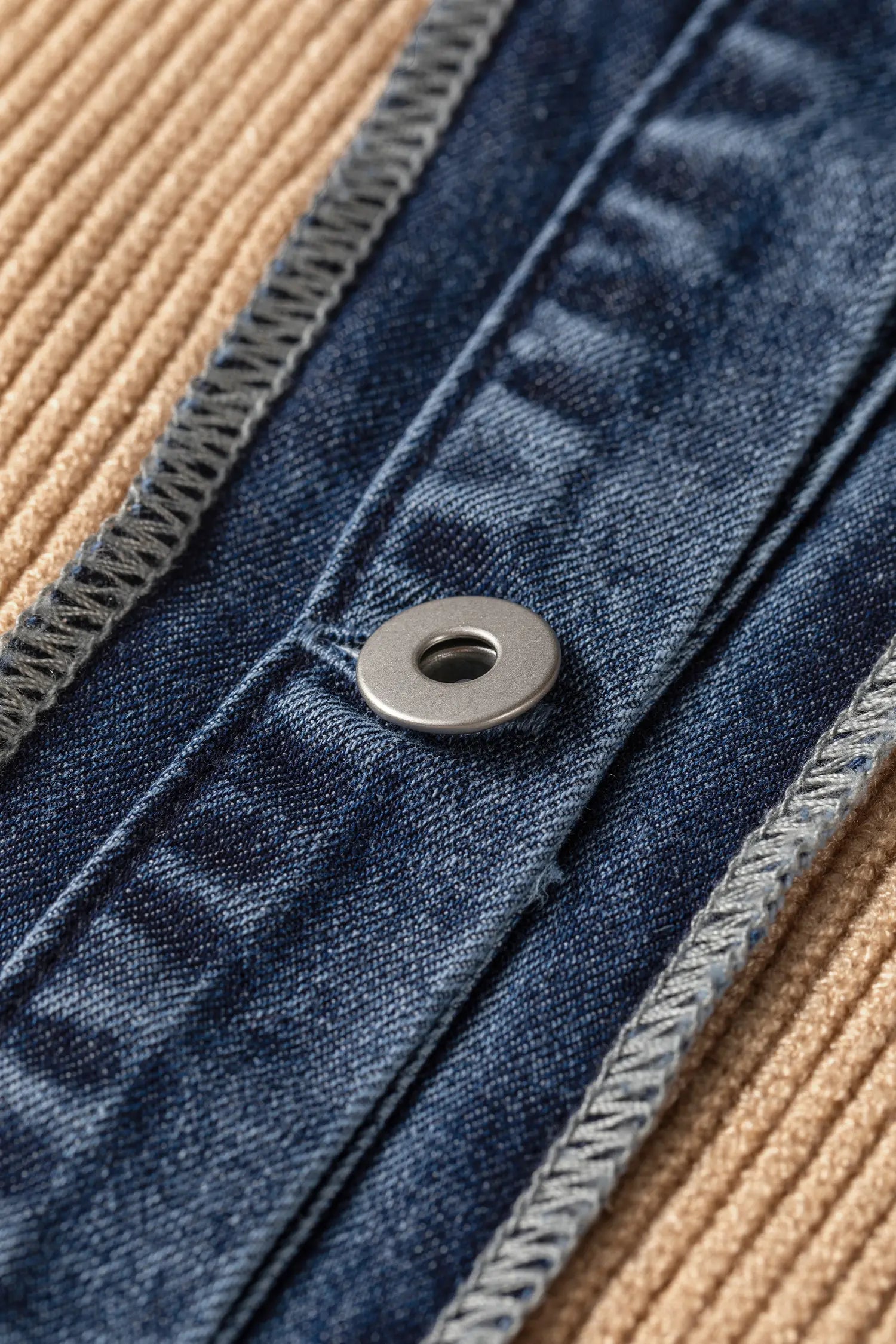 Close-up detail of a dark blue denim garment with a metal snap button and ribbed beige fabric border.