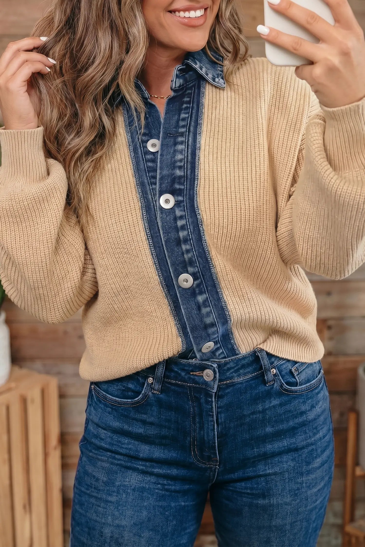 A woman wearing a beige ribbed knit sweater with a vertical dark blue denim placket and matching denim collar, paired with blue jeans, in a warm indoor setting.