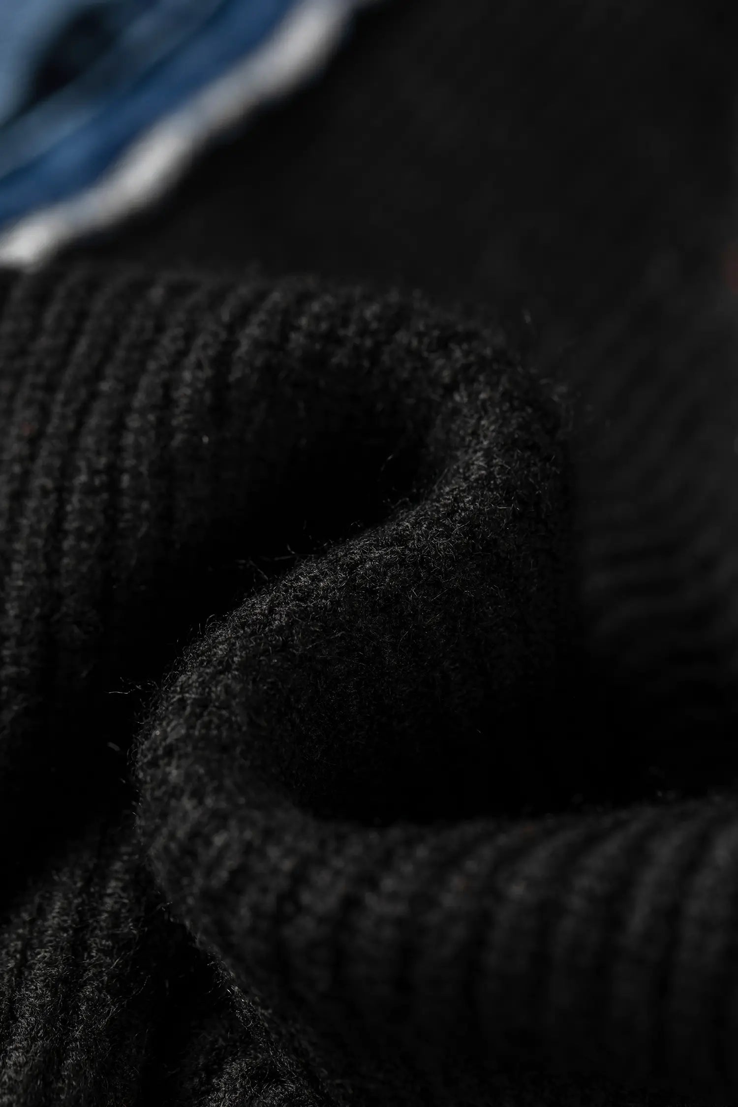 Close-up of a black ribbed knit fabric, showing the texture and folds of a sweater or garment.