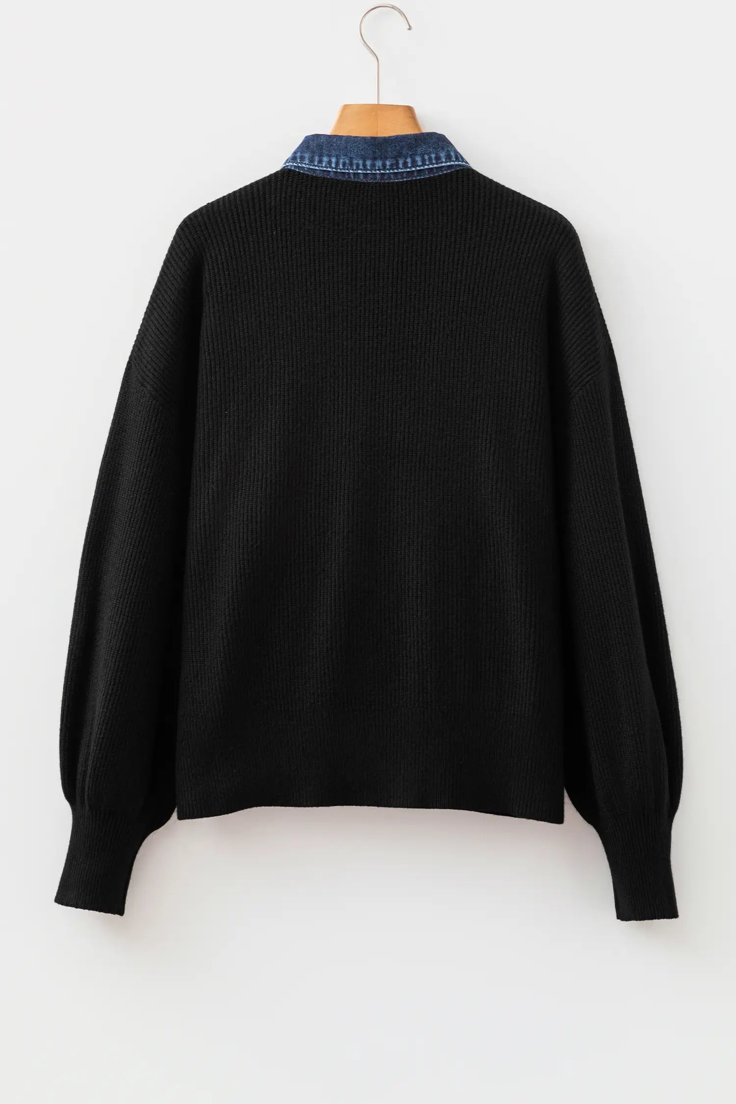 A black ribbed knit sweater with balloon sleeves, hanging on a wooden hanger against a plain white background. The back of the sweater features a contrasting blue collar with white lettering.