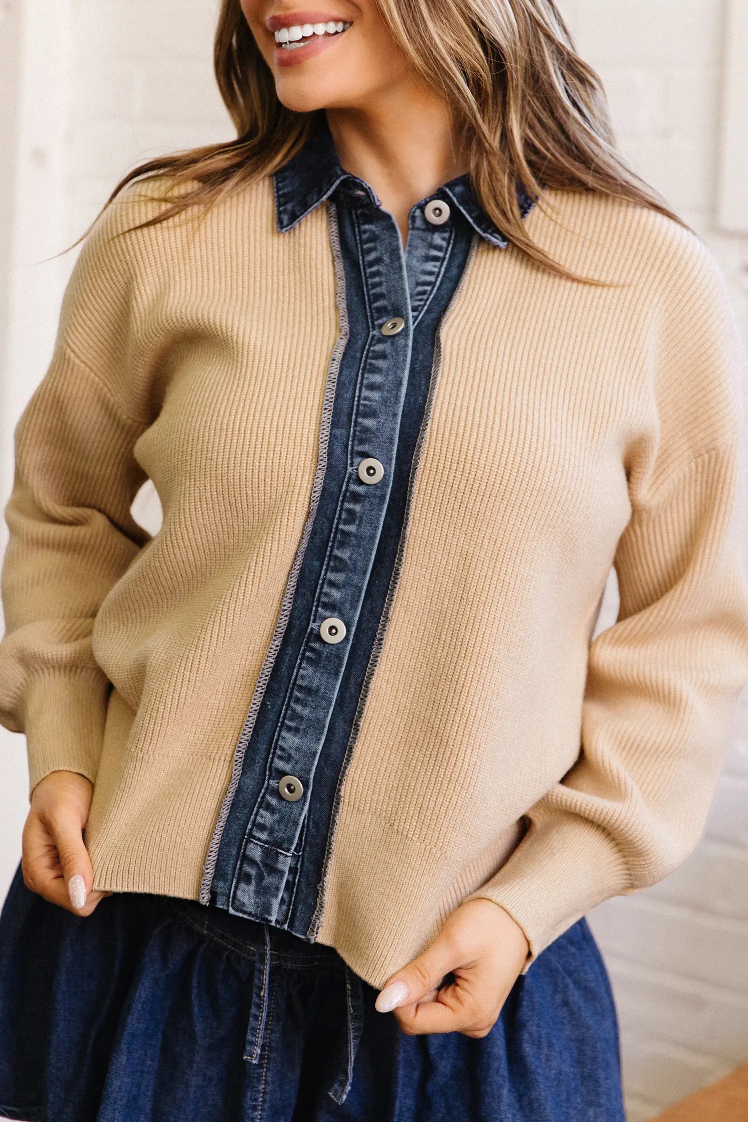 A woman wearing a beige ribbed knit cardigan with dark blue denim placket and collar details, paired with a dark blue skirt.
