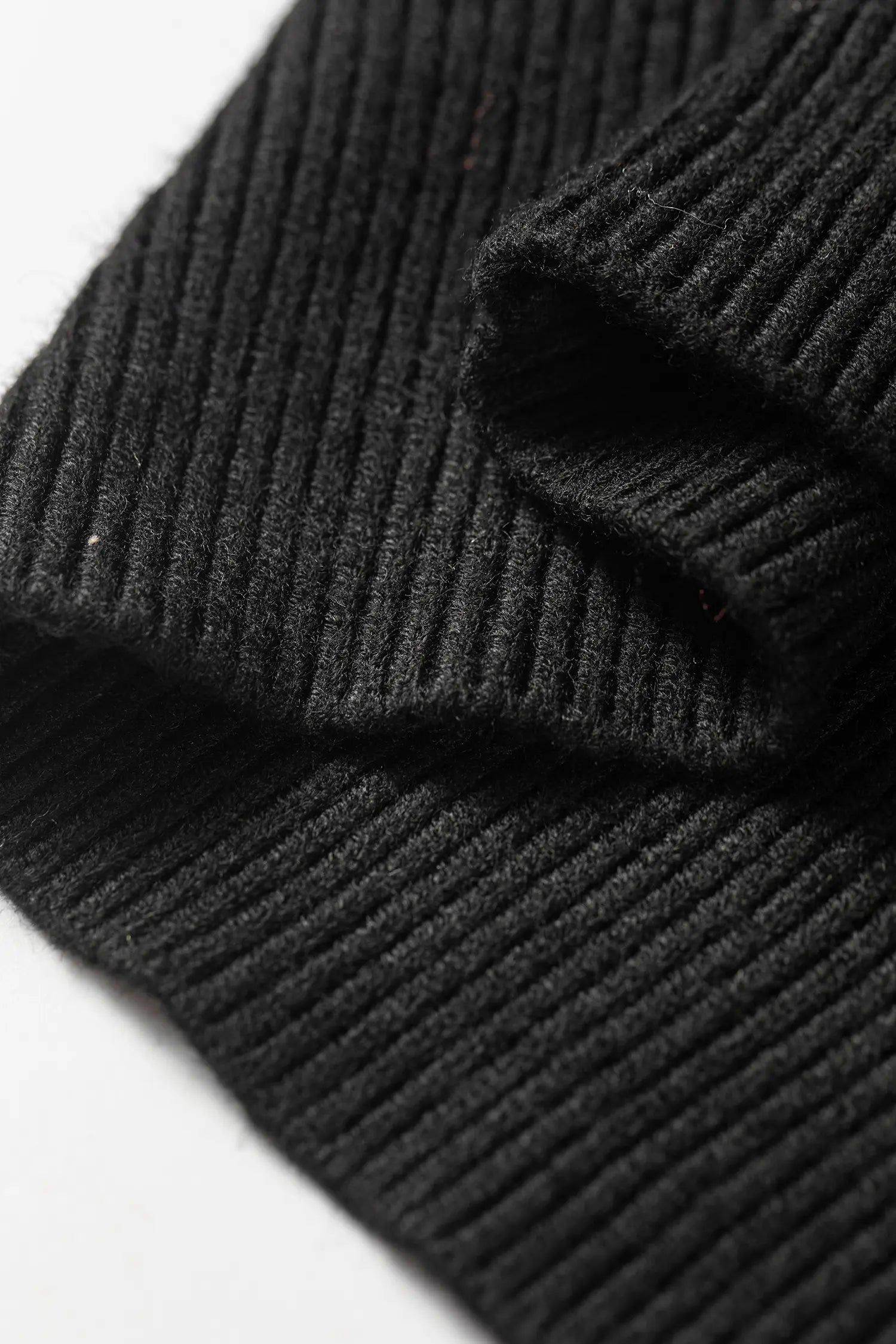 Close-up of a black ribbed knit fabric, showing the detailed texture and folds of the material against a plain white background.