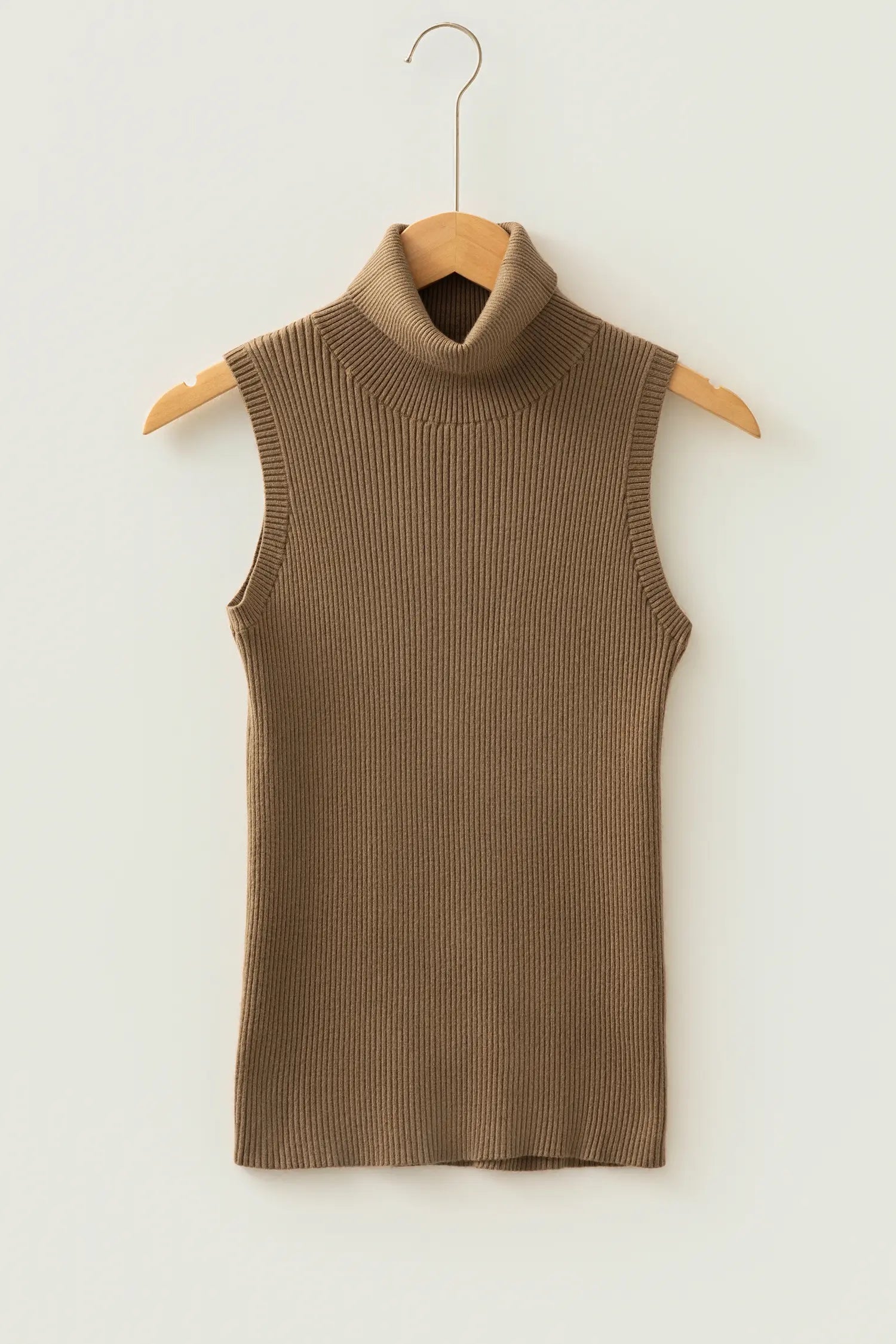 A sleeveless ribbed knit turtleneck sweater vest in a warm taupe-brown color, hanging on a wooden hanger against a plain off-white wall.
