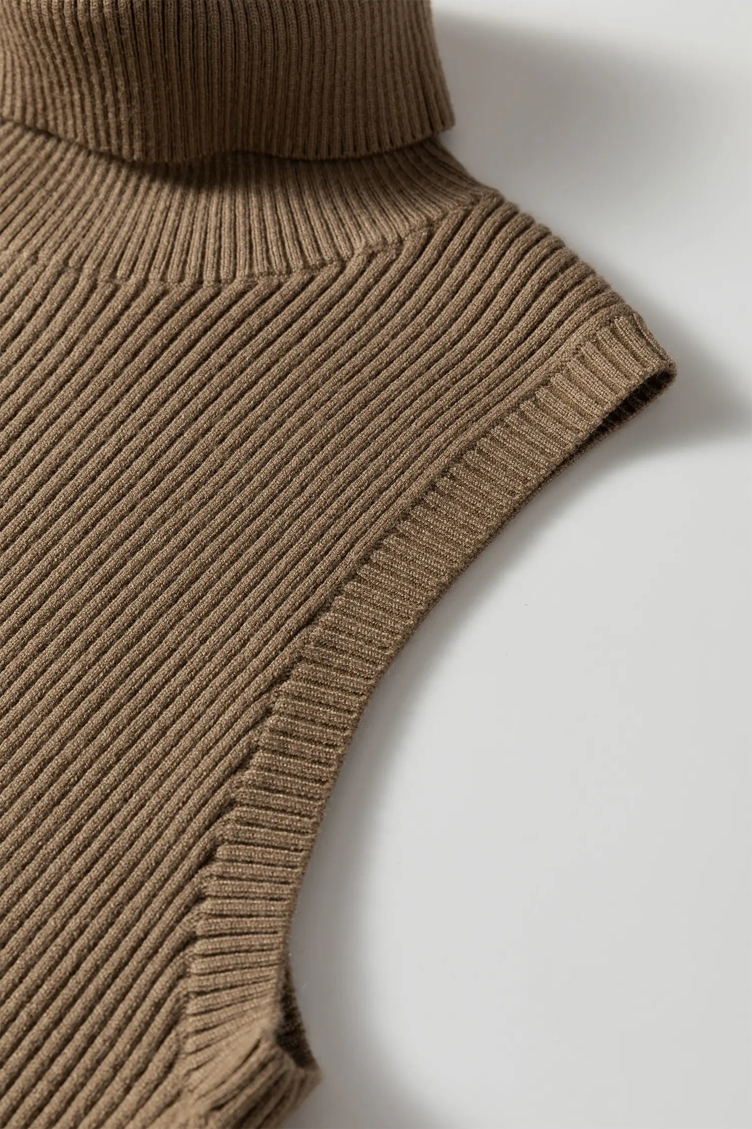 Close-up of a ribbed knit sleeveless top in a warm taupe-brown color, showing the texture and collar detail against a light gray background.