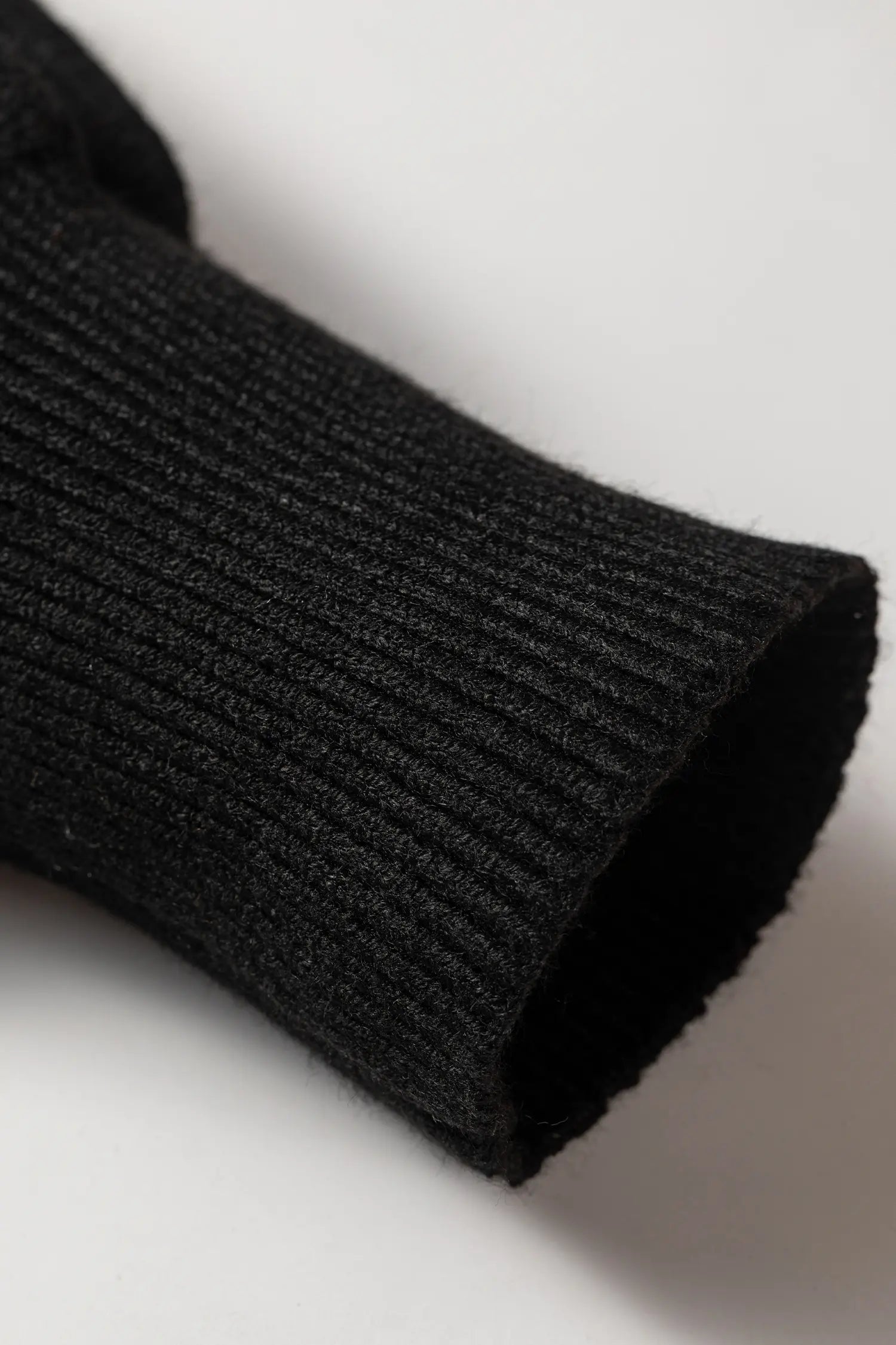 Close-up of a black ribbed knit sleeve or cuff, showing the texture and folded hem, on a light gray background.