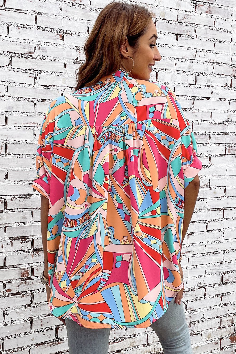 Woman wearing a colorful patterned shirt against a white brick wall.