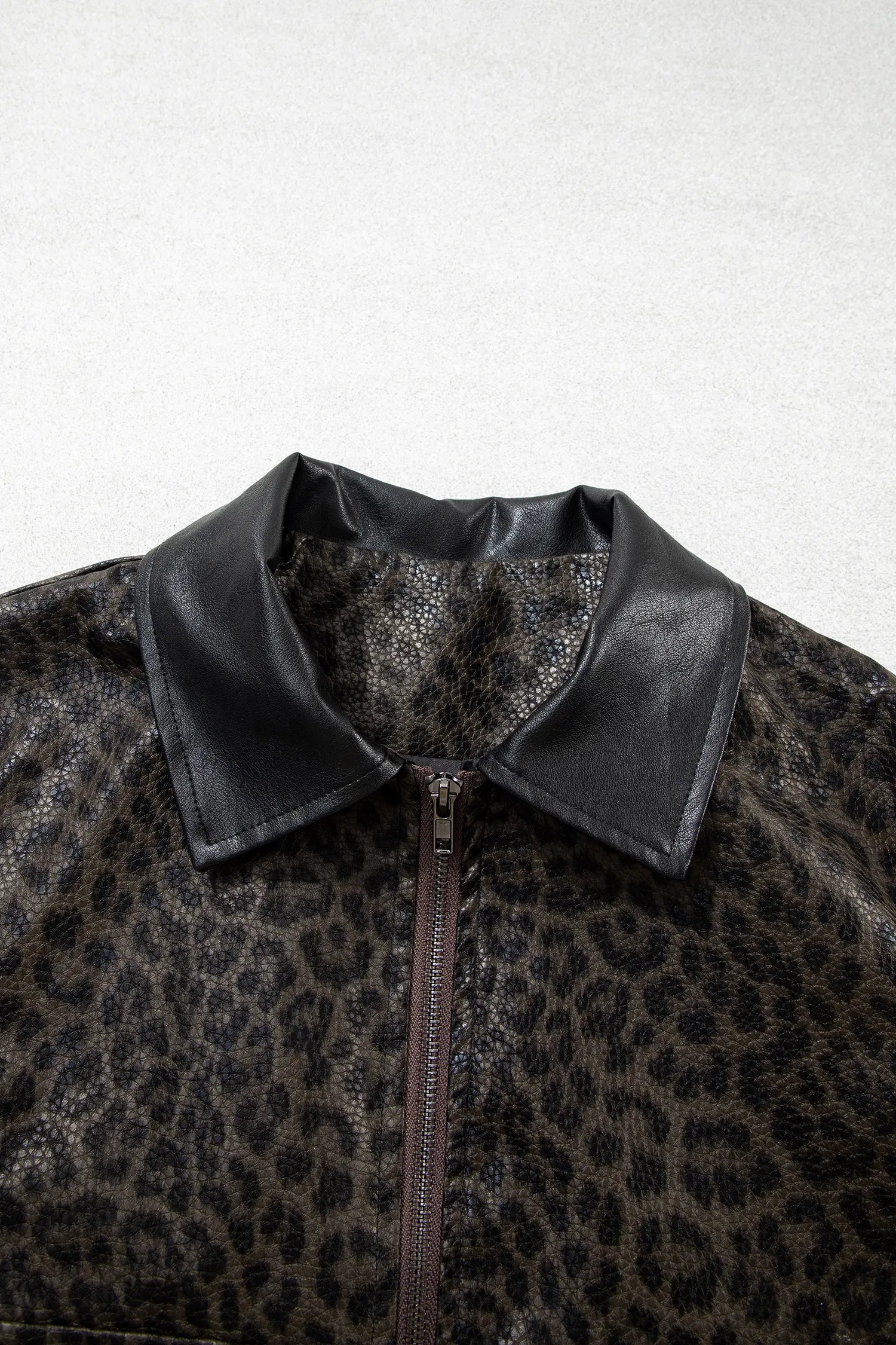 Close-up of a leopard-print jacket with a black faux-leather collar and a front zipper, shown against a light gray background.