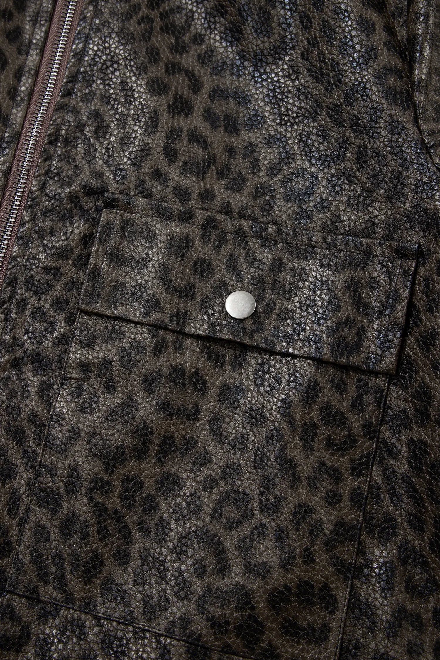 Close-up of a textured animal print jacket featuring a brown and black leopard pattern, a front flap pocket with a silver snap button, and a zipper along the left side.