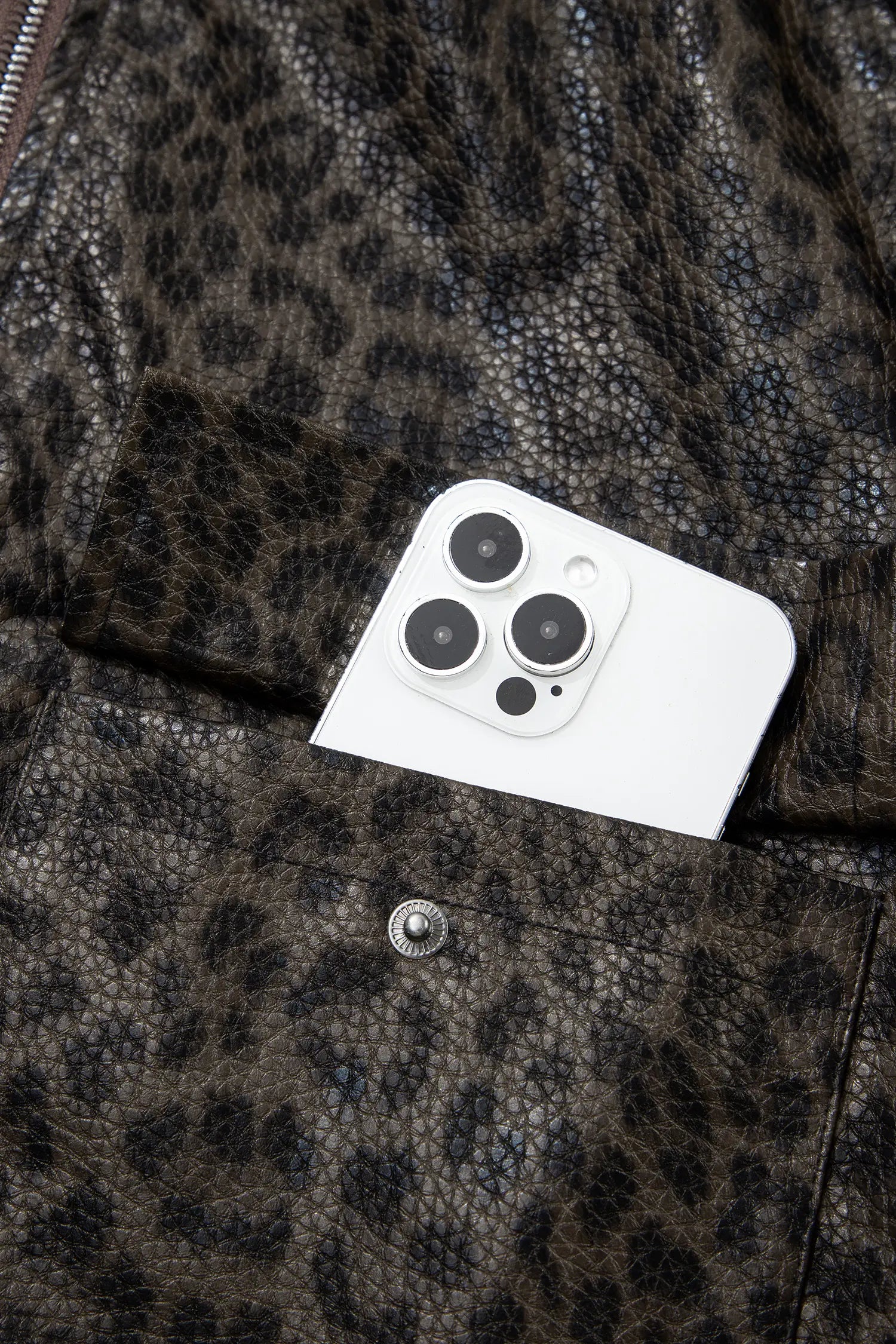 Close-up of a leopard-print faux leather jacket with a white smartphone tucked into a front pocket.