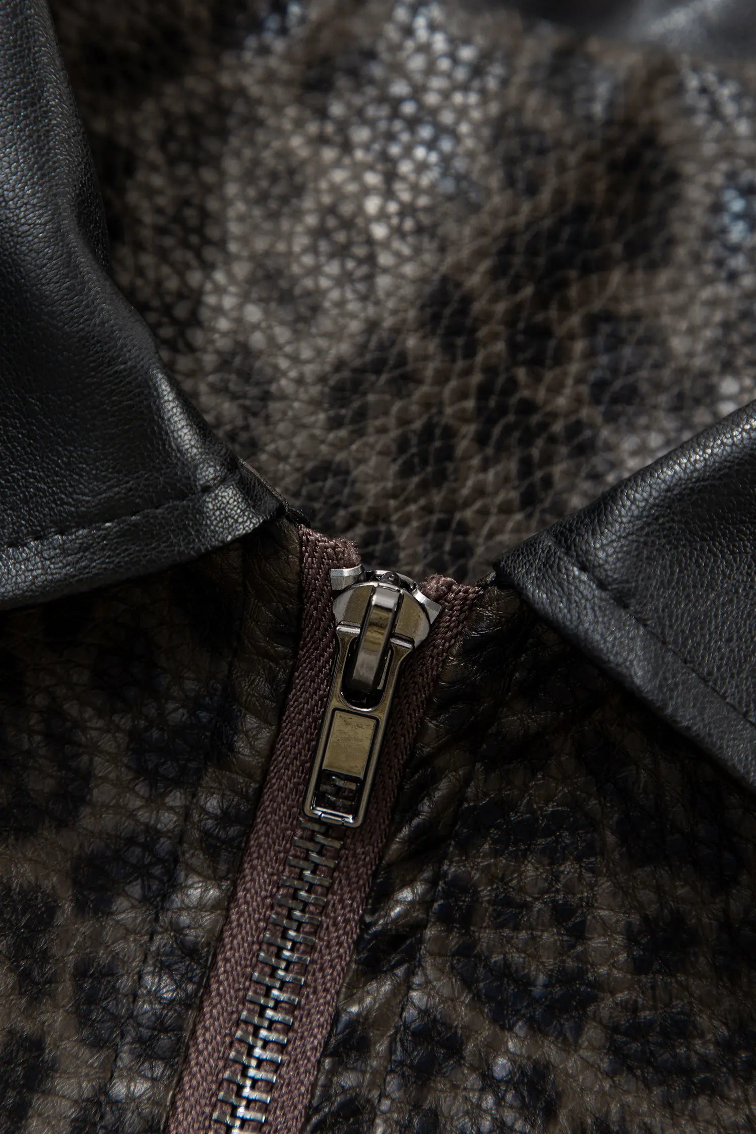Close-up of a collar with black leather trim and a brown and black leopard-print faux leather body, featuring a silver metal zipper.