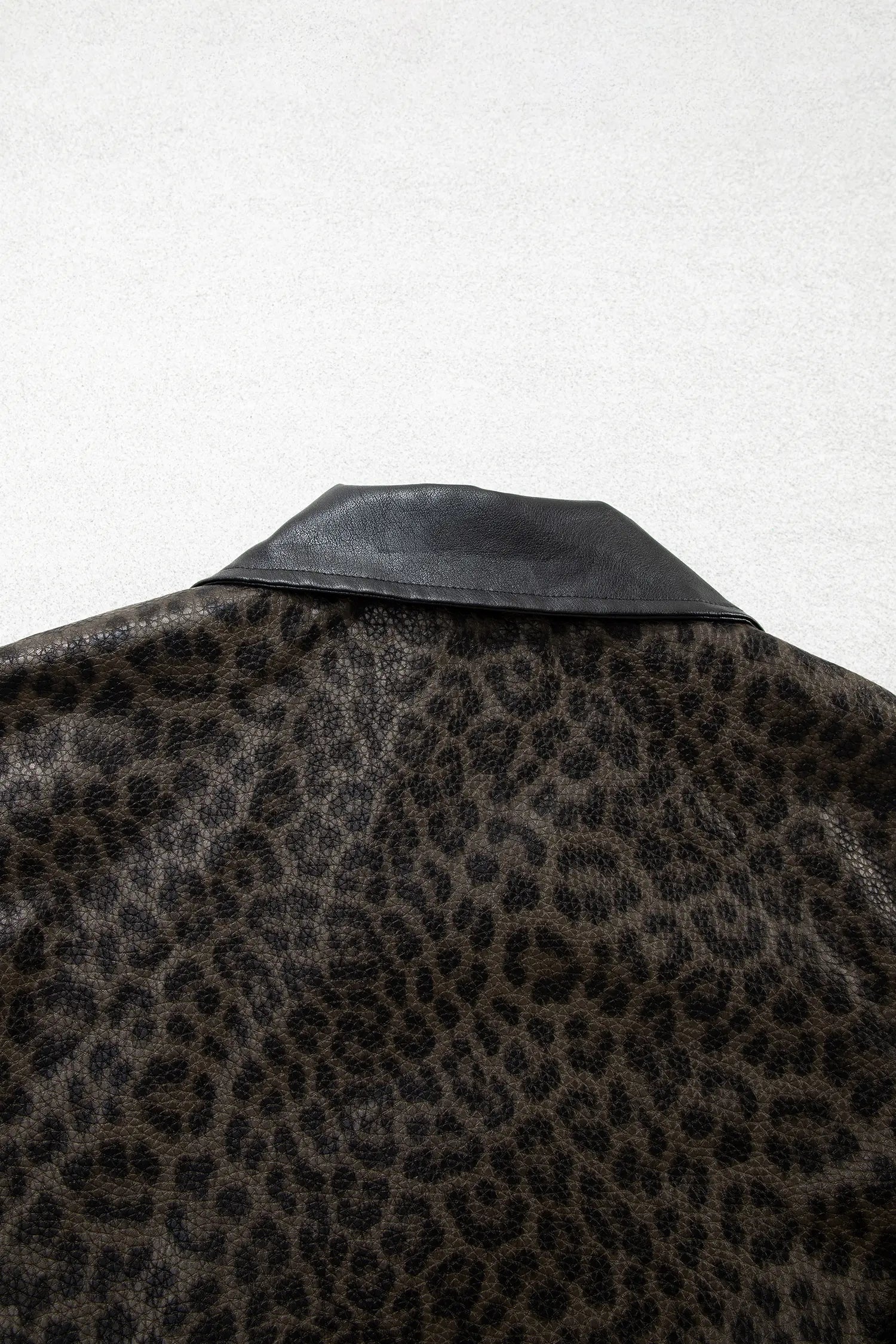 Close-up of a leopard-print jacket or shirt collar in black and brown, with a smooth black leather-like lapel or collar detail against a light gray background.