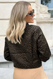 A woman with blonde hair and sunglasses, viewed from the back, wearing a dark brown and black leopard print bomber jacket and beige pants.