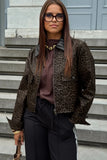 A woman wearing a brown and black leopard print jacket over a dark brown top, paired with black pants and glasses, standing on outdoor stone steps.